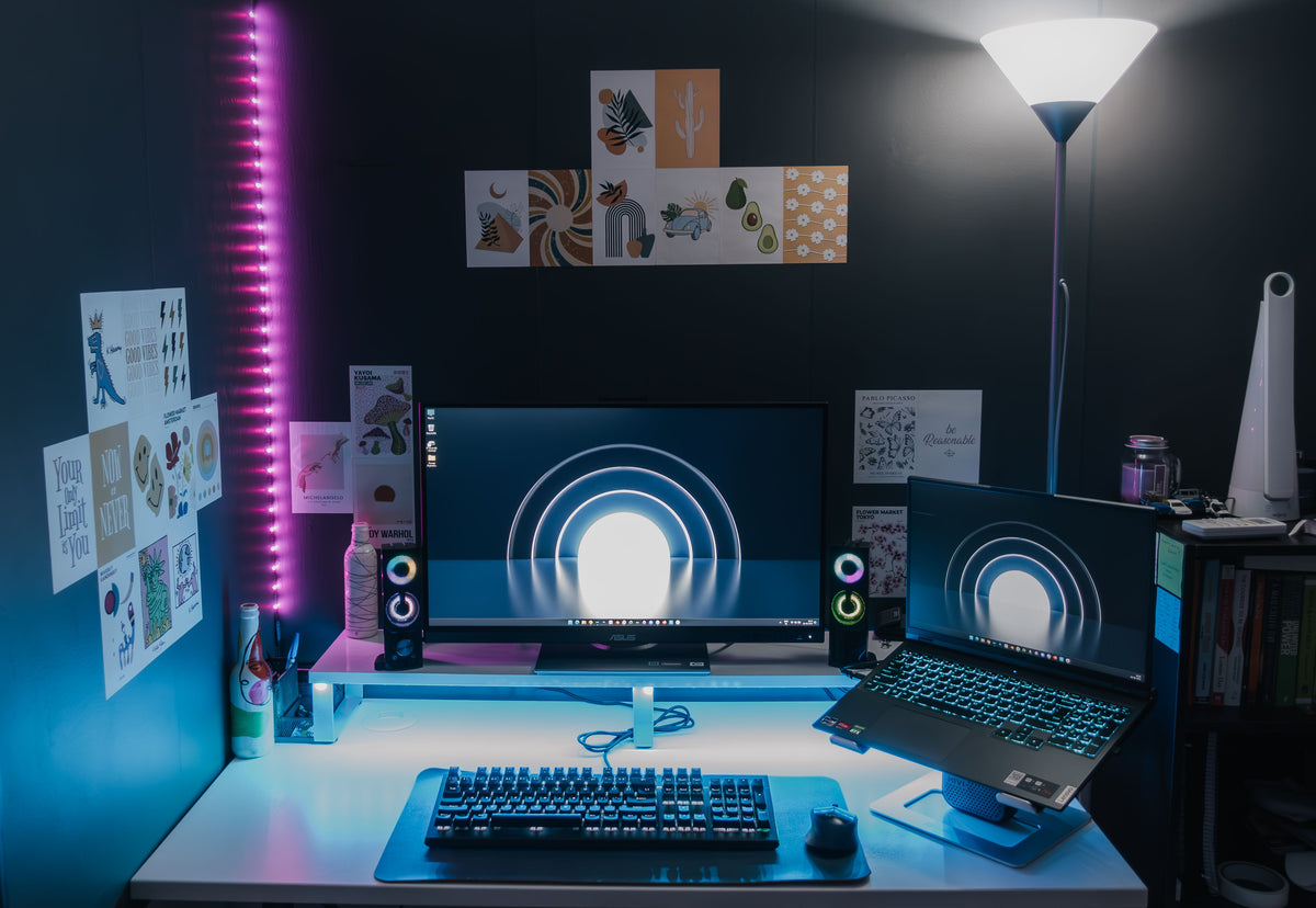 Room with RGB LED strip lighting behind a desk and monitors