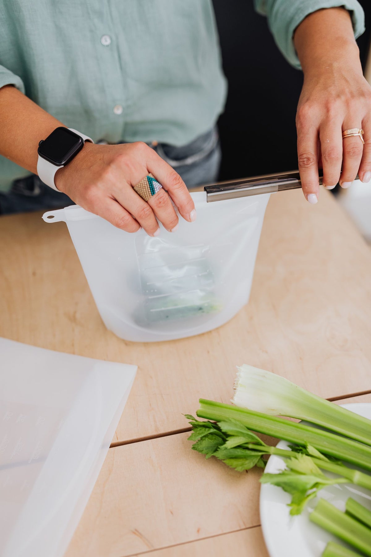 Hands sealing a reusable silicone food storage bag on a kitchen table